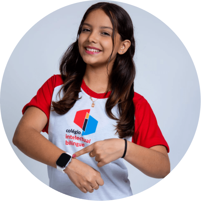Aluna sorrindo, de uniforme do Colégio Intelectual Bilíngue, apontando para o relógio