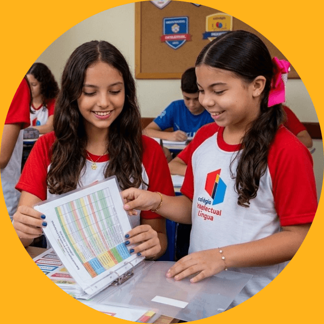 Duas alunas do Colégio Intelectual Bilíngue, de uniforme, sorrindo enquanto olham um caderno