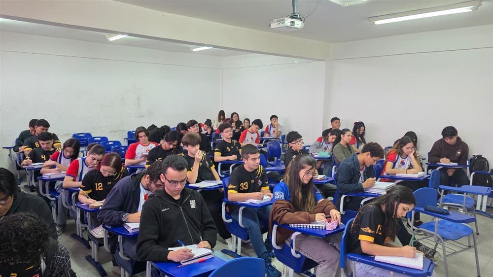 Estudantes em sala de aula, sentados em carteiras azuis