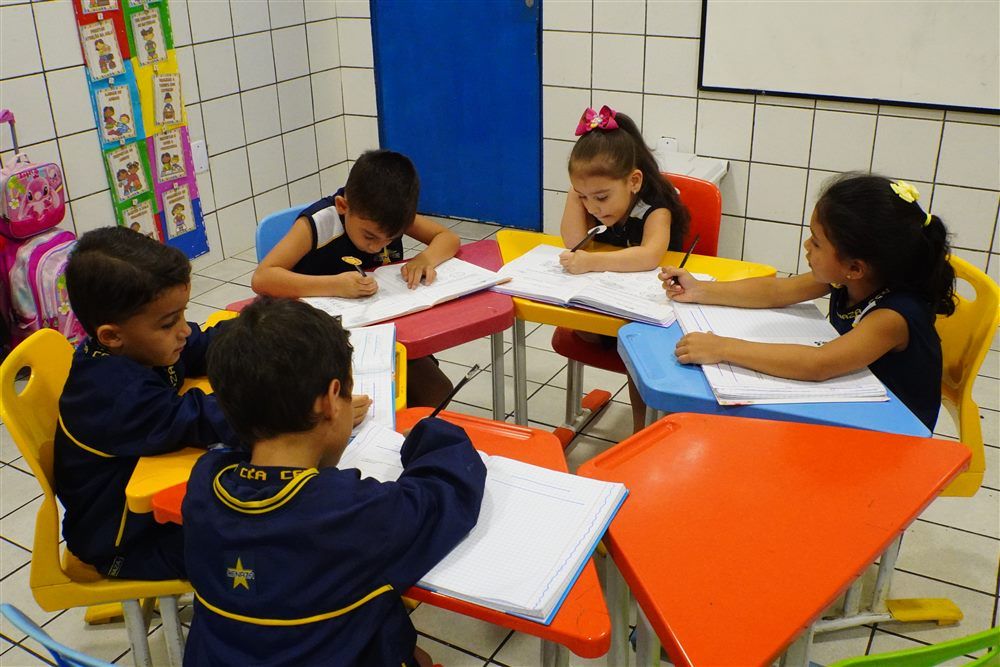 Crianças pequenas escrevendo em mesas coloridas