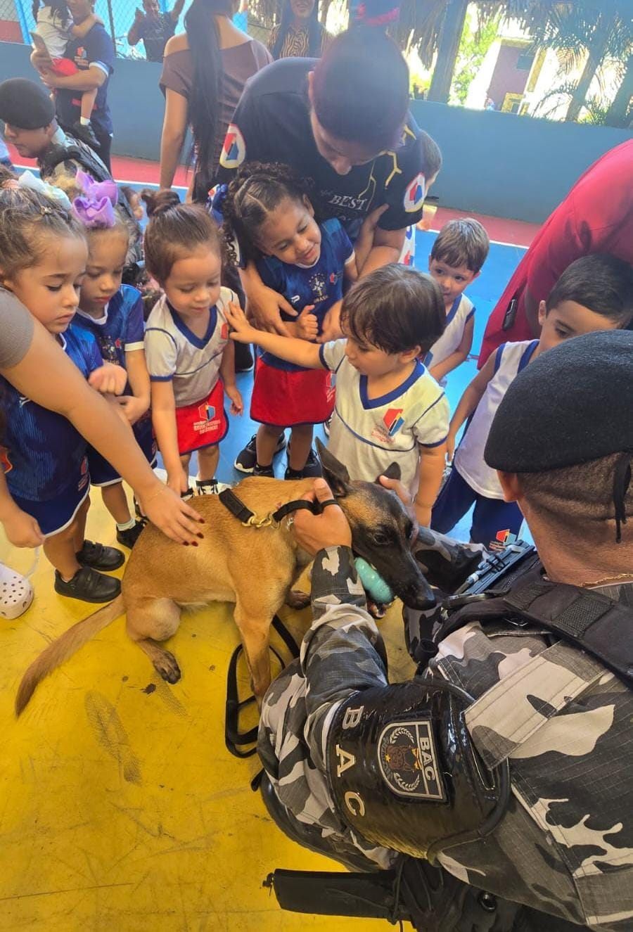 Crianças ao redor de um cão e de um policial, no ginásio