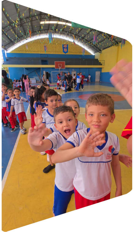 Crianças uniformizadas acenando no ginásio da escola