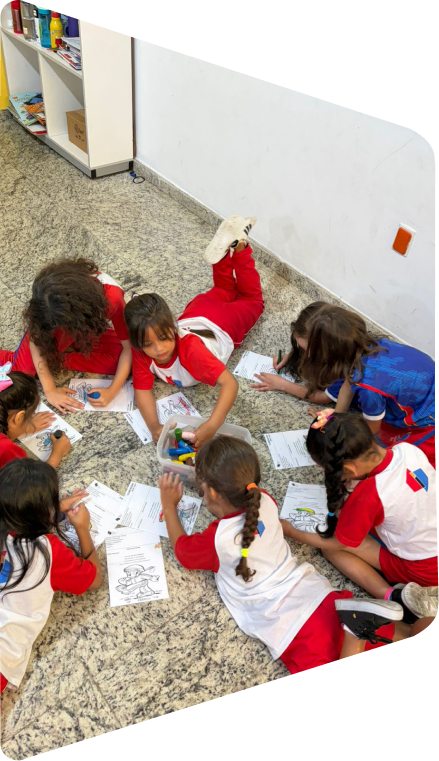 Crianças da Educação Infantil desenhando no chão da sala, com uniforme branco e vermelho